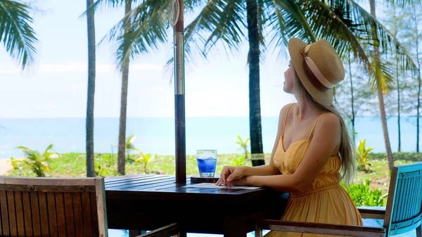 Tropical vacation. Smiling happy woman in hat sitting in outdoor seaside cafe — Stok Foto