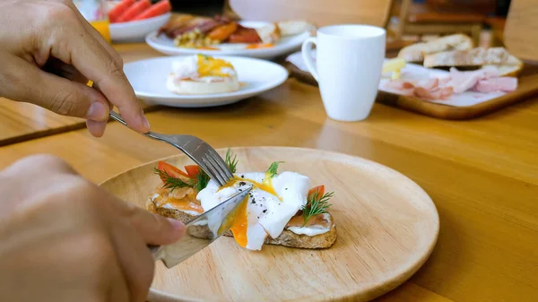 Male hands with fork and knife cut egg benedict with liquid yolk on toast — Fotografia de Stock
