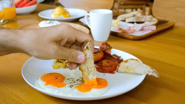 Male hand dip bread in fried egg yolk in restaurant or cafe, breakfast or lunch — Fotografia de Stock