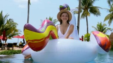 Mayo giyen mutlu kadın eğleniyor ve şamandıralarda dinleniyor şişme tek boynuzlu at yatağında.