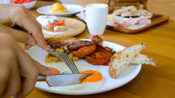 Male hands with fork and knife cut, eat fried eggs with liquid yolk on breakfast — Stok fotoğraf