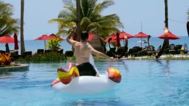 Mutlu adam lüks oteldeki yüzme havuzunda şişme tek boynuzlu atın üstünde, tatilin ya da güneşli yaz günlerinde tatilin tadını çıkarsın. Bilinmeyen komik yetişkin erkek turist. Arka plan