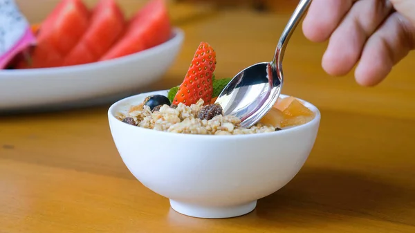 Human hand with spoon eat healthy breakfast food, bowl of granola with yogurt — Stock Photo, Image