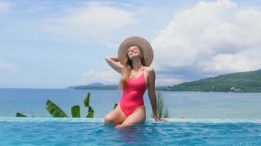 Kırmızı mayo, güneş şapkası ve havuz kenarında dinlenen su dolu sağlıklı ciltli seksi kız.