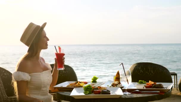 Piękna dziewczyna nosić kapelusz cieszyć się wakacje patrząc na morze, grzywny jadalnia zestaw żywności — Wideo stockowe