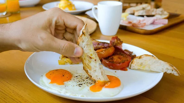 Man hand dip toasted bread in fried egg yolk in restaurant on breakfast or lunch — Fotografia de Stock