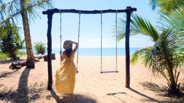 Woman with hat enjoying freedom on swing in Phuket, Thailand. Travel concept