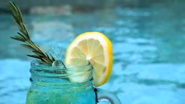 Limon dilimli kokteyl bardağı, yüzme havuzunun yanında biberiye. Tatil, yaz