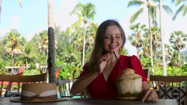 Νεαρή ευτυχισμένη ταξιδιωτική γυναίκα χαλαρώστε στο καφέ με φρέσκια καρύδα στην παραλία — Αρχείο Βίντεο