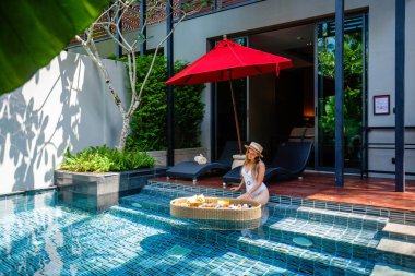 Beyaz mayo giyen mutlu kadın lüks havuzda kahvaltı yapıyor.