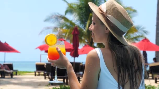 Привлекательная молодая туристка пьет освежающий коктейль в бассейне, наслаждается морем, пальмами и видом на пляж. Счастливая улыбчивая девушка отдыхает на курорте с безалкогольным напитком. Пхукет, Таиланд. — стоковое видео