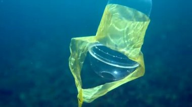 Plastik bardakla kristal mavi suda güneş ışınlarında yüzen plastik bir bardağın sualtı videosu. Çevresel plastik kirliliği sorunları kavramı. Dünya okyanus günü. Okyanustaki çöp..