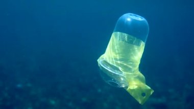 Plastik bardakla kristal mavi suda güneş ışınlarında yüzen plastik bir bardağın sualtı videosu. Çevresel plastik kirliliği sorunları kavramı. Dünya okyanus günü. Okyanustaki çöp..