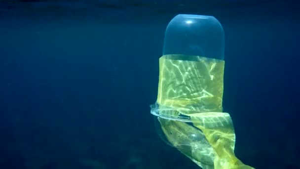 Podvodní video plastového koktejlového kelímku s plastovým držákem plavajícím v křišťálově modré vodě ve slunečních paprscích. Koncept problémů znečištění životního prostředí plasty. Světový den oceánu. Koš v oceánu. — Stock video