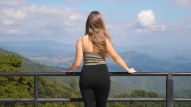 Kadınlar dağlara bakmaktan hoşlanırlar. Dişi gezginlerin arka plandaki yeşil tepelerle birlikte doğada dinlenmesi. Zinde gezgin kadın güneşli ve sakin günün tadını çıkarıyor.