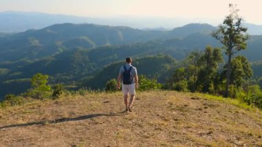 Yeşil dağ manzaralı tepede yürüyen gezgin bir gezginin arka görüntüsü. Erkek doğa yürüyüşü. Seyahat yaşam tarzı ve macera konsepti.