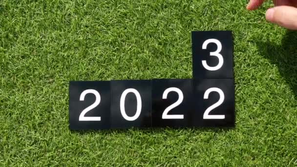 2023年あけましておめでとうございます 2022 2023年変更 人間の手は緑色の芝生の上で2022年から2023年までの数字でプラスチック板を変え 2番を削除します さようなら2022 2023へのこんにちは 介護環境の概念 — ストック動画