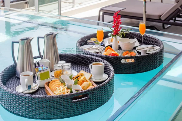 Drijvende dienbladen met ontbijt in zwembad. Influencer of blogger genieten van exotisch eten in luxe hotel spa. Vers exotisch voedsel met fruit. Luxe vakantie in de zomer. — Stockfoto