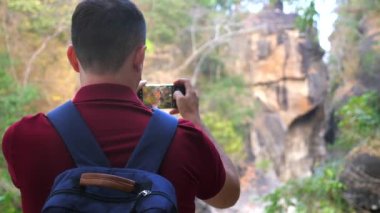 Dağ yürüyüşü fotoğrafçısı ya da video blogcusu cep telefonuyla kanyon çekiyor. Sırt çantası olan bir gezgin. Akıllı telefon panoramik kamerasıyla manzarayı ve doğayı yakalamak. Arka plan