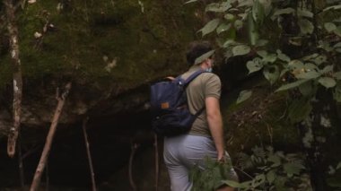30 'lu yaşlarda maskeli bir erkek orman parkında yürüyor. Macera ve seyahat, sırt çantalı adam tropik barışçıl ayyaşların arasında yürüyüş yapıyor. Ekoloji konsepti. Orman parkında gezgin turist.