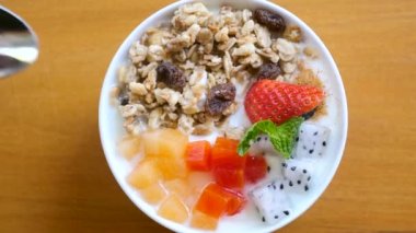 Bir kase ev yapımı tahıllı yoğurt, kuru üzüm, taze böğürtlen, çilek, doğranmış kavun ve tahta masada papaya. Kaşıklı kadın eli sağlıklı kahvaltı yemeği yer. Temiz yemek. Üst Manzara. Yakın plan..