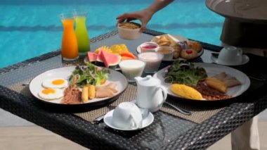 Lüks oteldeki restoranda kahvaltı servisi yapan Asyalı bayan garson. Garson el, tropik tatil beldesindeki açık havuz kafeteryasında sabah yemeği ve içecekler koydu. Seyahat, tatil, tatil konsepti