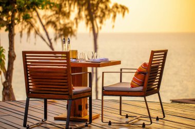Teraslı modern lüks restoranda deniz batımı. Sahilde bir çift sandalyesi olan açık hava restoranı. Tropikal plaj restoranında masa ayarı. Şık bir otel ya da restoran..