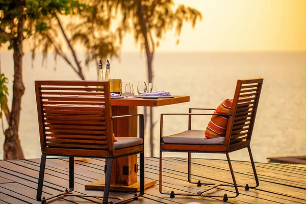 Teraslı modern lüks restoranda deniz batımı. Sahilde bir çift sandalyesi olan açık hava restoranı. Tropikal plaj restoranında masa ayarı. Şık bir otel ya da restoran..