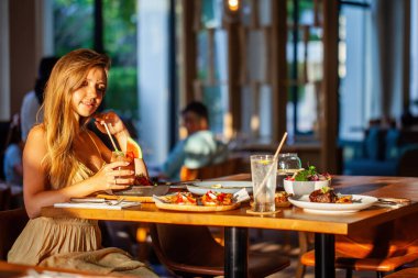 Güzel ve mutlu bir kız gün batımında lüks bir restoranda romantik bir akşam yemeği yiyor. Uzun saçlı çekici bir kadın kafede öğle yemeğinde lezzetli yemekler yiyor..