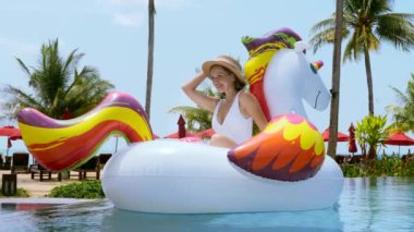 Genç ve mutlu bir kadın, tropik tatil beldesinde yaz tatilinde. Seyahat eden kız ya da nüfuzlu biri yüzme havuzunda şişme tek boynuzlu at oyuncağıyla güneşleniyor. Tatil, güneşli gezi, yaz tatili konsepti.