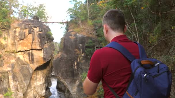 タイの国立公園で素晴らしい自然のカジュアルな旅行ブロガーの撮影ビデオ バックパック付き30代の森林ハイカー写真家の男のビューは 携帯電話上のソーシャルメディアのための峡谷のビデオを作る — ストック動画