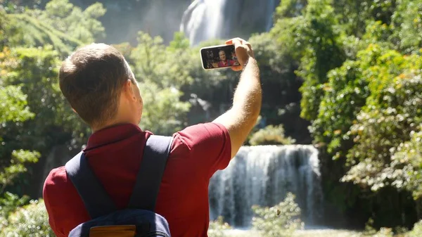 Young man vlogger, blogger record selfie movie on his smartphone outdoors, looking at camera, talk on video, shoot blog on phone at nature. Concept of influencer clip to social media or content maker.