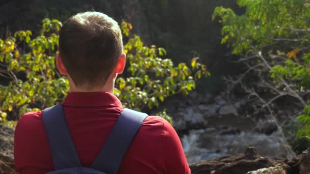 山の端に立っているバックパック付きの旅行者の男性のバックパックビューと日没の渓谷で自然の川の景色をお楽しみください 景色の良い森の中の男性ハイカー 自由と冒険の概念 — ストック動画