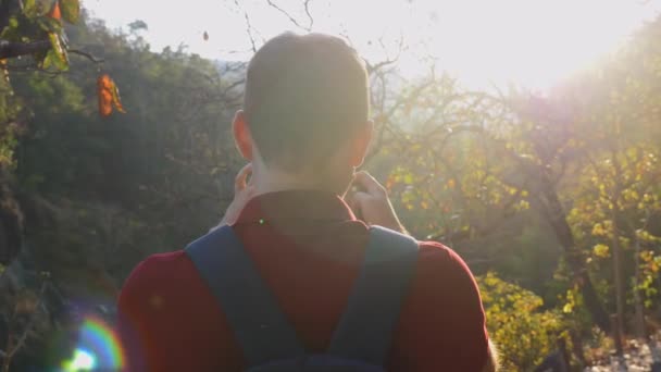 自然景観の撮影写真や携帯電話でビデオでバックパックを持つ若い観光客の男 森林ハイカーの写真家やソーシャルメディアの影響力のある人々のバックビュー レンズフレアとサンビーム — ストック動画