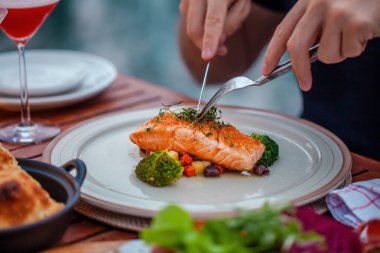 Lüks yemekteki adam, açık hava restoranında taze deniz ürünleri, soğuk kesimler ve kokteyl bardaklarıyla servis ediliyor. Adam elleri ızgara somon kesiyor. Sağlıklı yemek.