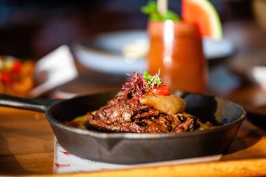 Lüks restoranda ahşap masada tavada taze pişmiş et. Sebzeli ızgara sığır eti ve arka planda soğuk içecek. Güzel yemek..