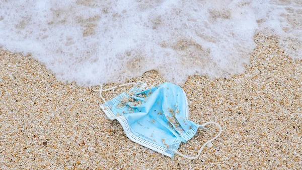Environmental and ocean pollution concept during Covid pandemic. Discarded to ocean coronavirus single-use face mask. Used medical face mask washed away by the ocean wave
