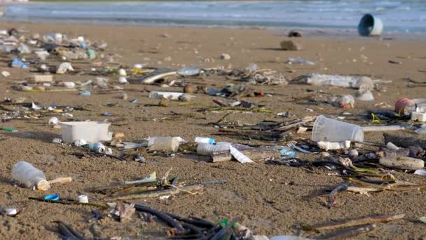 海のビーチでプラスチック汚染 背景に海の波で満潮時の廃棄物 海洋プラスチック汚染 ゴミの種類 ペットボトル 海辺の袋 — ストック動画