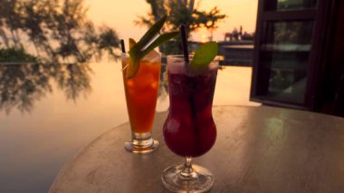 Tropikal oteldeki açık havada lüks bir restoranda gün batımında tatil yapan çifte moktail. Akşam alacakaranlıkta barda kokteyllerle dinlenmek. Seyahat, seyahat, tatil, yaz tatili konsepti..