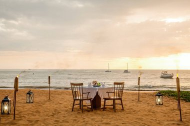 Sahilde romantik bir günbatımı yemeği. İki kişilik masa balayı, lüks yemekler, deniz manzaralı restoranda şampanya bardakları ve arka planda yatlar. Yaz tatili ya da düğün konsepti.