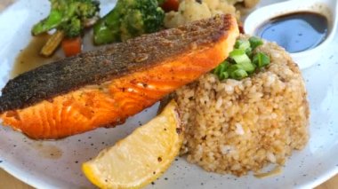 Kızarmış sarımsaklı pilav, baharat ve sebzeli ızgara somon filetosu. Sağlıklı deniz ürünleri zengini Omega-3. Limonlu ve soslu ızgara somon balığı bifteği..