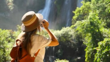 Asya 'da seyahat eden bir kadın. Elinde fotoğraf makinesi olan kadın gezgin güzel bir tropik şelale vuruyor. Seyahat tutkusu gezisindeki genç turist kızın sinematik videosu. Keşif ünlü yer.