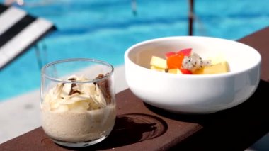 Sağlıklı vejetaryen yemeği - papaya, ejderha meyvesi ve elmalı egzotik meyve salatası, müsli yulaf ezmesi, badem fıstığı ve kuru üzüm. Tropikal tatil, havuz ve güneş şemsiyeleri üzerine sağlıklı bir kahvaltı.