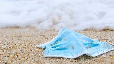 Coronavirus COVID-19 salgınından beri deniz sahilindeki atık kirliliği. Arka planda okyanus dalgası olan yüz maskesi. Koronavirüs sırasında çevre ve okyanus kirliliği.