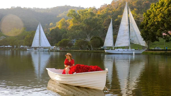 Woman in red dress sailing on wooden boat against sunset at mountain top. Romantic scene of perfect date. Romance and activities for in love people. Celebration of Happy Valentines day.