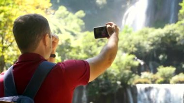 Genç başarılı blog yazarı ya da video blogcusu akıllı telefondan özçekim videosu kaydediyor, kameraya bakıyor, filme konuşuyor, doğada telefon üzerinden blog çekiyor. Sosyal medya etkileyicisi, içerik üreticisi kavramı.
