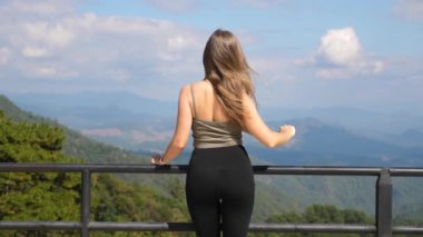 Kadınlar dağlara bakmaktan hoşlanırlar. Dişi gezginlerin arka plandaki yeşil tepelerle birlikte doğada dinlenmesi. Zinde gezgin kadın güneşli ve sakin günün tadını çıkarıyor.