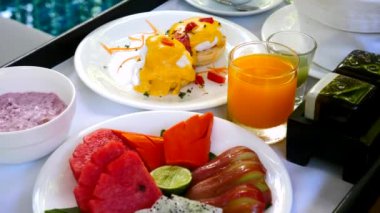 Kahvaltı tatil köyünde ya da özel yüzme havuzunun yanındaki otelde servis edilir. Benedict yumurtalı tepsi, taze pasta, meyve suyu ve bilardo masasında kahve fincanı. Yaz seyahati, tatiller, tatil kavramı.