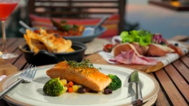 Lüks oteldeki açık hava restoranında yemek masasında servis edilmiş. Güzel bir İtalyan lokantası. Izgara somon ve brokoli seramik tabakta çatal bıçak, Focaccia, kokteyl, soğuk et..