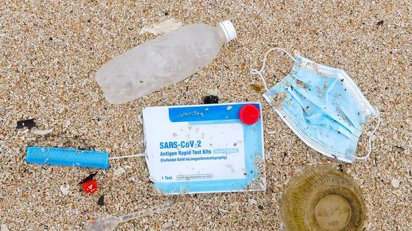 Ocean plastic pollution. Used medical face mask and Covid test on the sea beach. Waste during COVID-19. Discarded coronavirus single-use face mask and self tests on sandy beach